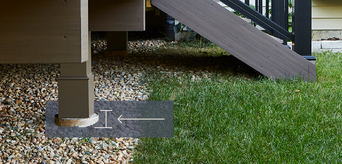 A close up of deck posts shows where the post is secured by a concrete footing in the ground.