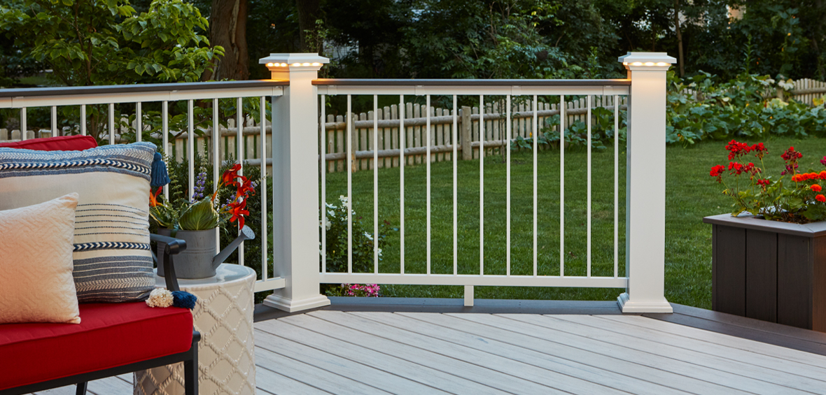A gray deck with seating leads into a backyard with a white deck railing and post lights centered.