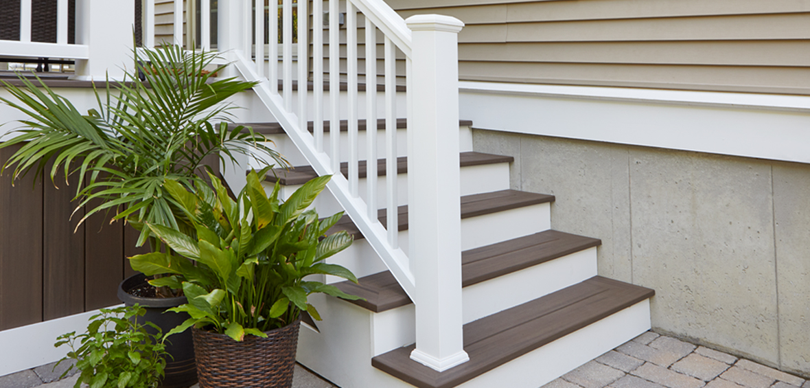 White and brown deck stairs transition from patio to deck with potted plants placed next to the railing.