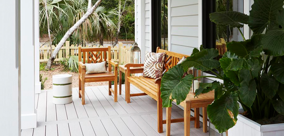 A small porch in the shade includes a wood seating set and a large potted plant looking out to the front yard. 