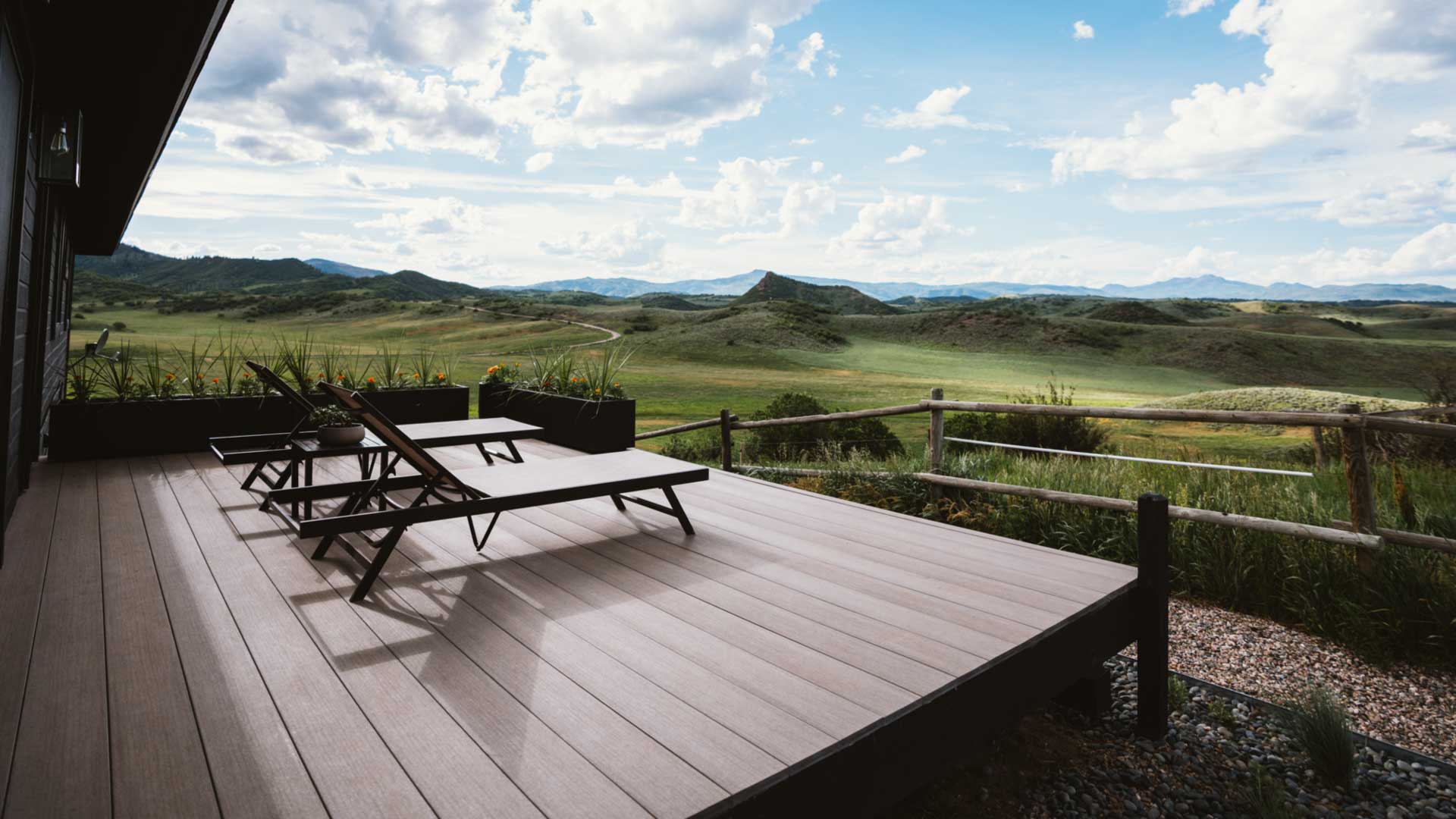 Two lounge chairs on a deck look out upon rolling hills in the Colorado landscape