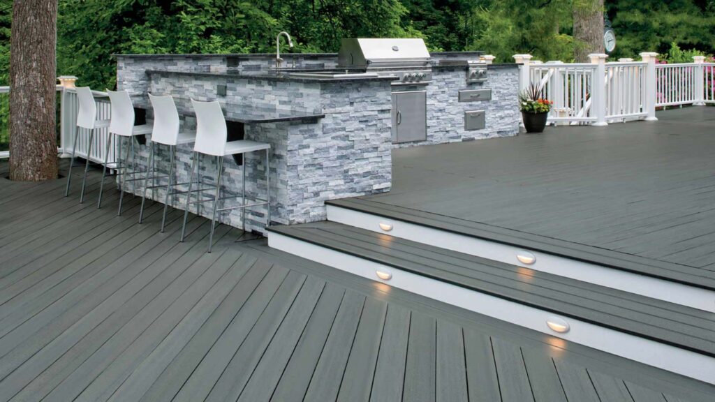 A medium gray deck features multiple levels and an outdoor grilling area separated by a one flight of stairs