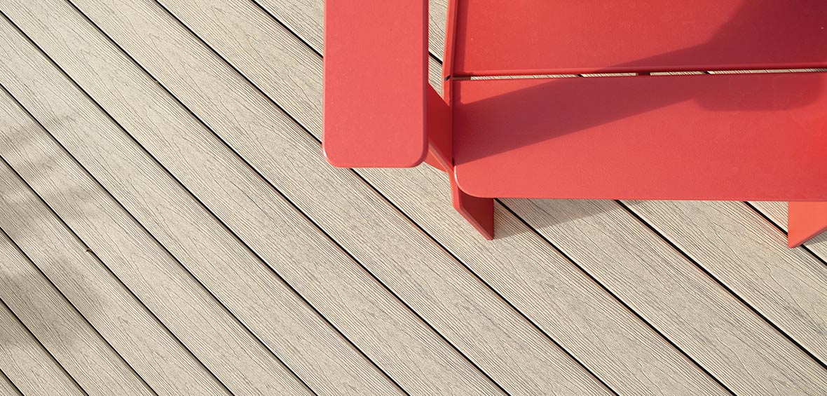 An overview close-up image of a beige composite deck includes the corner of a red outdoor chair. 