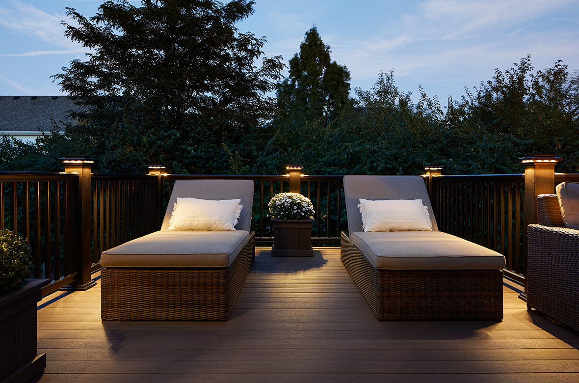 A deck at night with built-in lights surrounding two outdoor chaise loungers. 