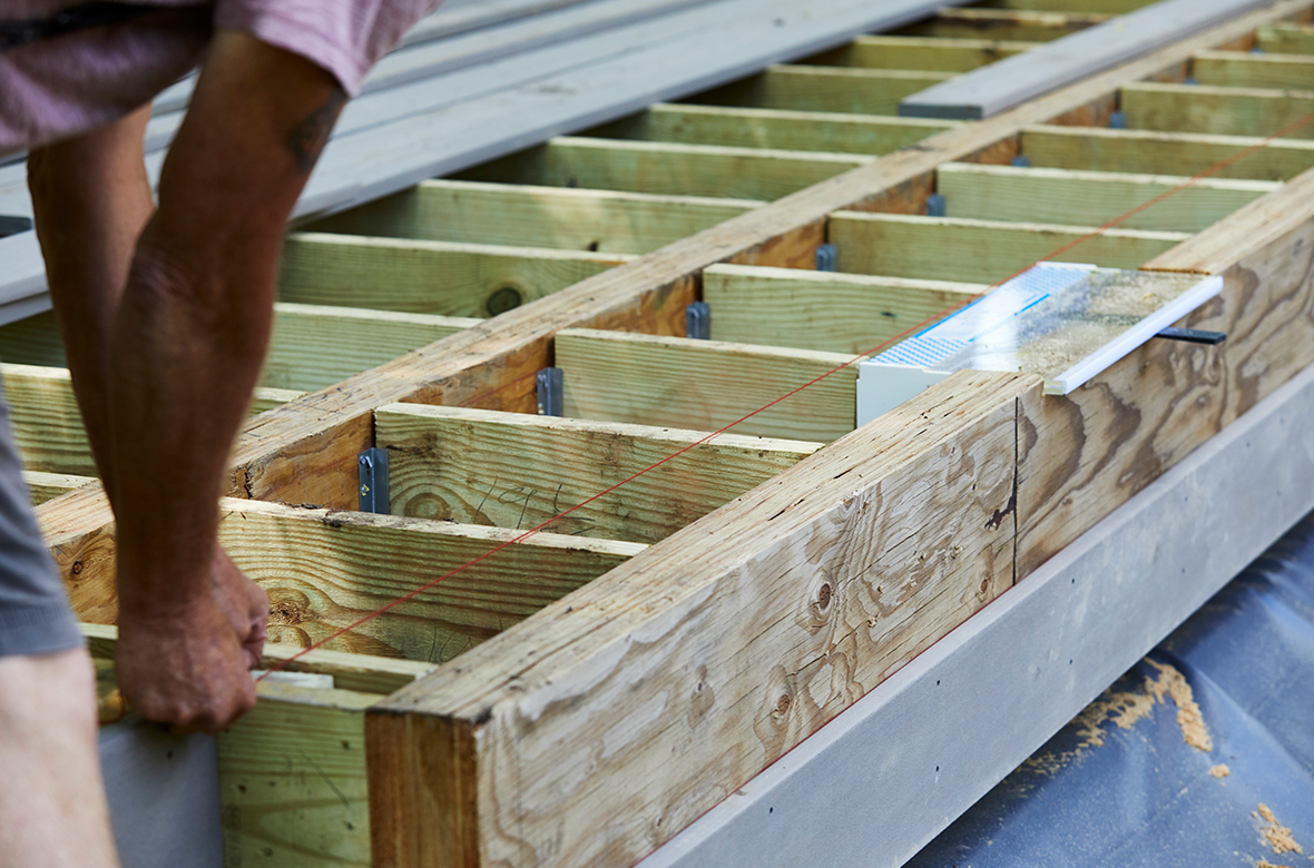 A builder uses a string line to mark a straight measurement on the top of a deck’s substructure joists.