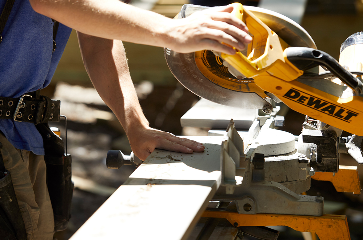 A contractor uses a power miter saw to cut a deck board to the correct length.