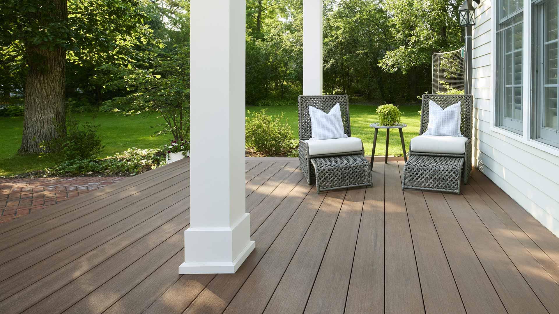 Two wicker chairs with pull out foot rests on a low-laying backyard deck