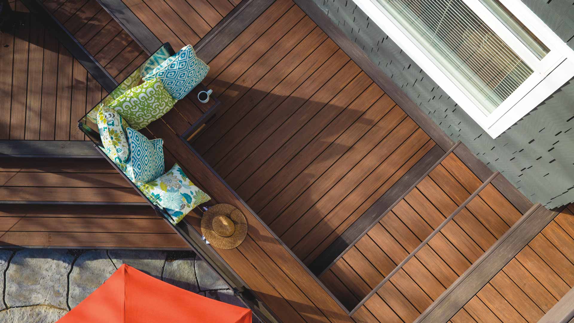 Overhead shot of pillows, a sun hat, and a coffee mug on a mahogany-colored deck