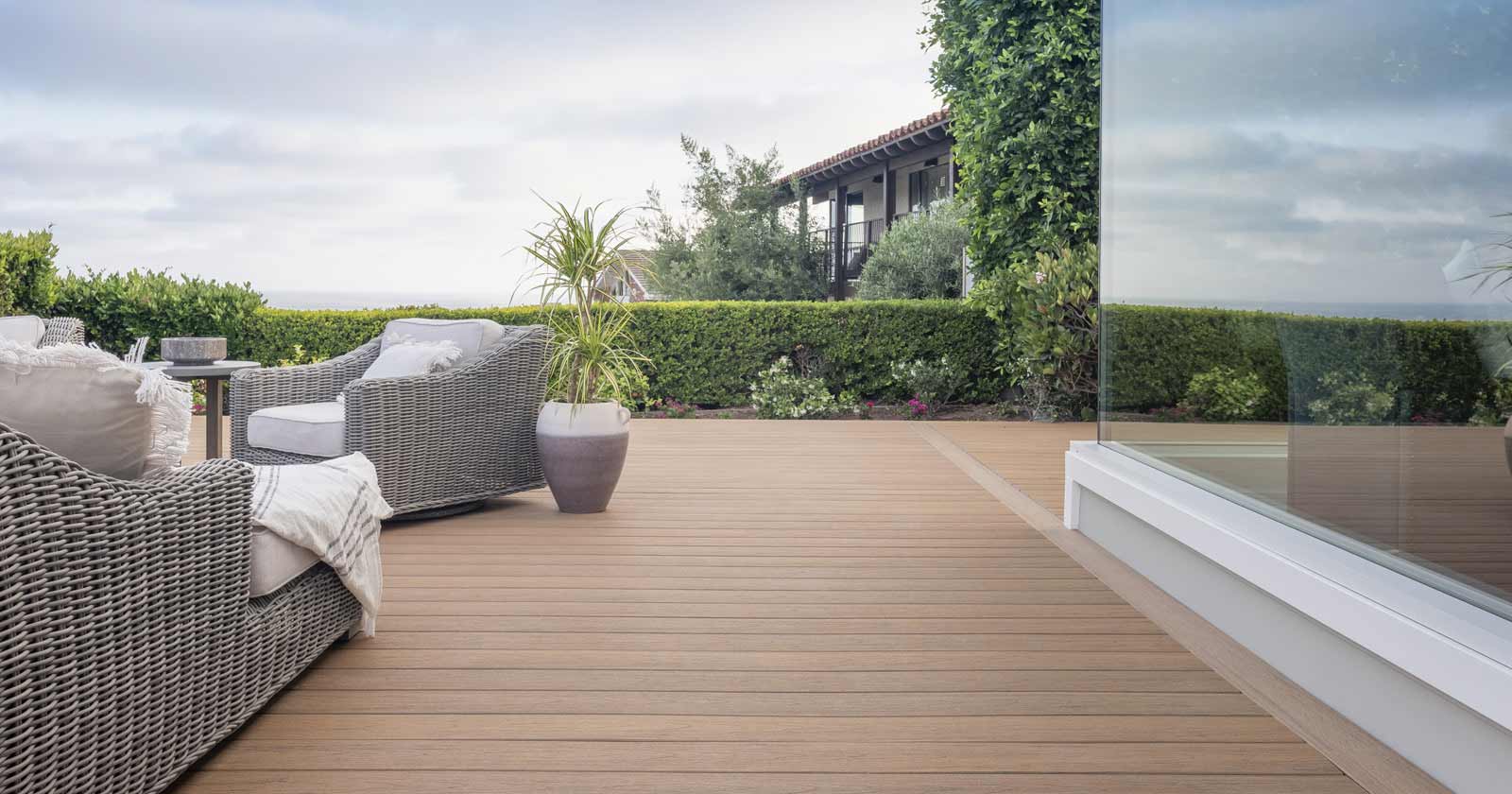 Patio furniture on a tab deck sits opposite to a full glass wall of a house