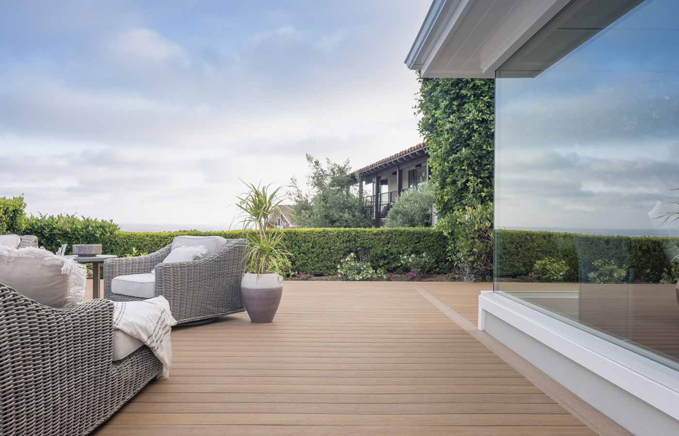 Patio furniture on a tab deck sits opposite to a full glass wall of a house