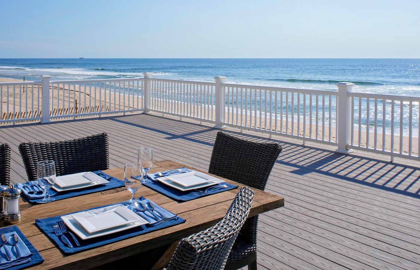 Set table on a gray deck overlooking a sandy beach