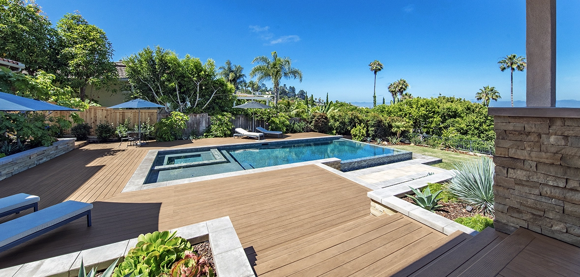 An in-ground pool and spa features a wraparound composite patio with deck furniture and landscaping. 