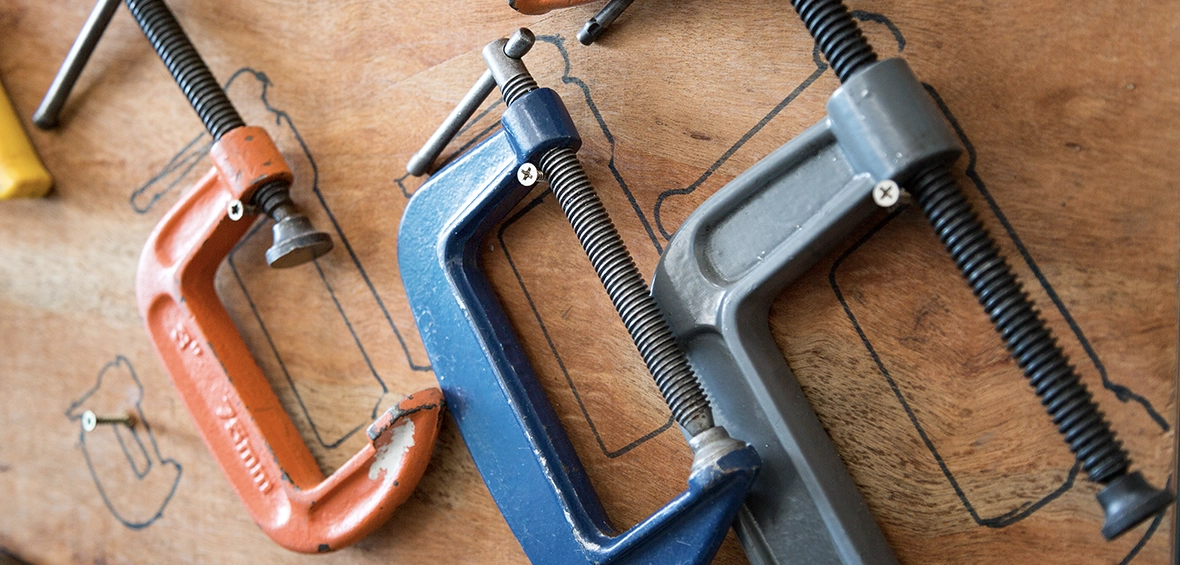 Three different-sized C-clamps hang on a wall above a workbench. 