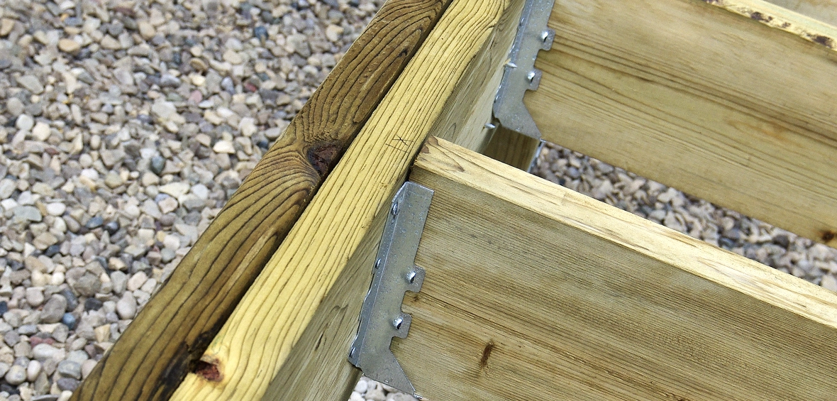 A close up of a deck connection shows joist hangers secured with outdoor screws. 