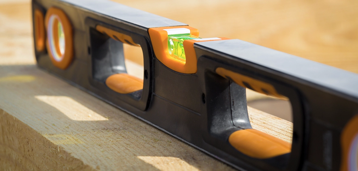 An orange and black level on top of a wood plank shows a balanced bubble in the green bubble window. 