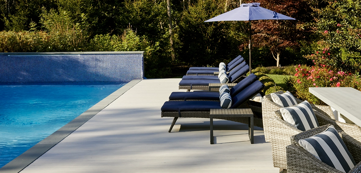 Deck chairs and loungers sit in a row on top of an in-ground pool patio.