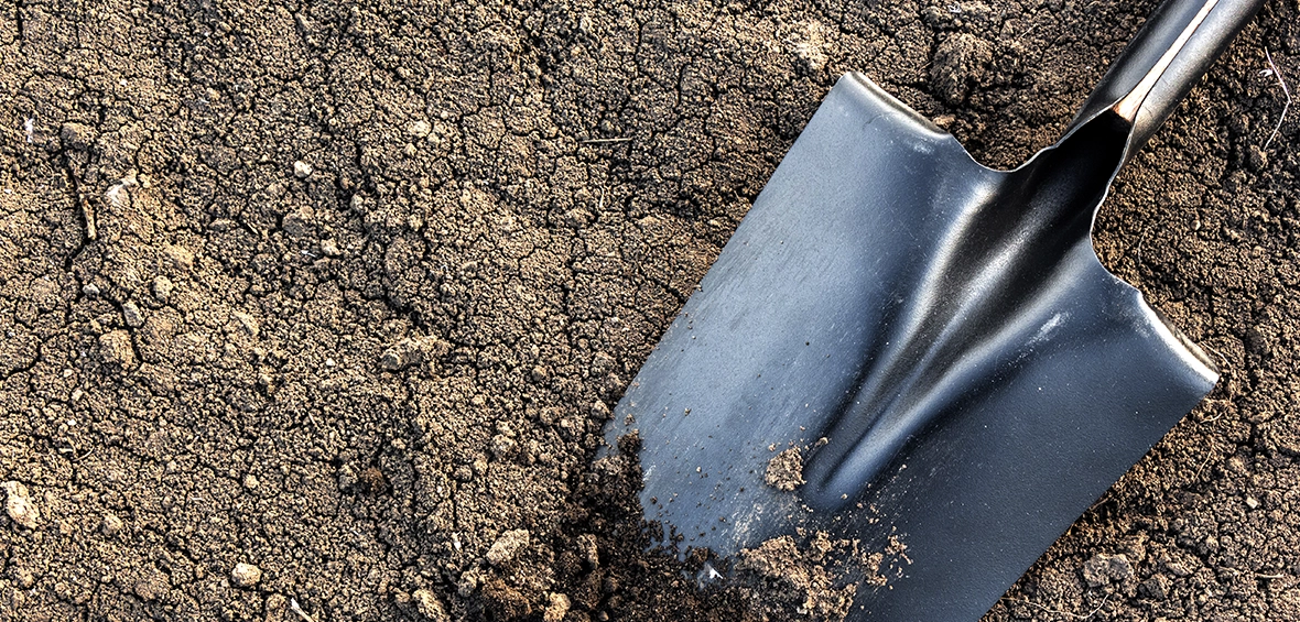 A black shovel is partially submerged in crumble soil.
