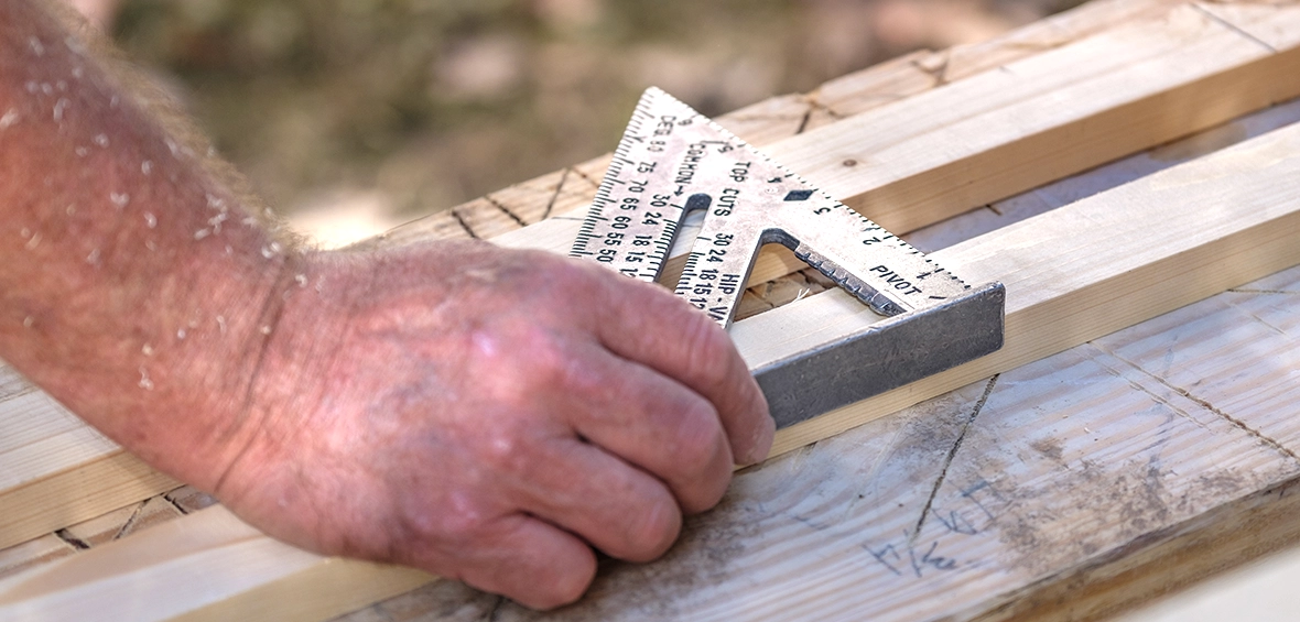 A hand holds a square at the edge of a board to measure it.