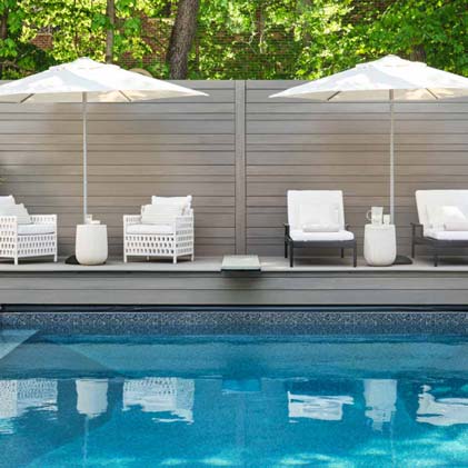 A poolside deck with two umbrellas and four white outdoor armchairs