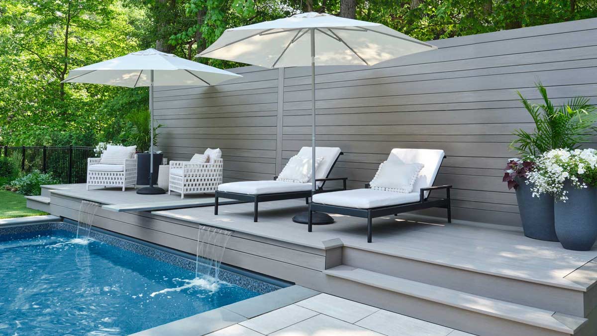 Angled side view of a light gray deck with multiple lounge and arm chairs chairs next to a pool
