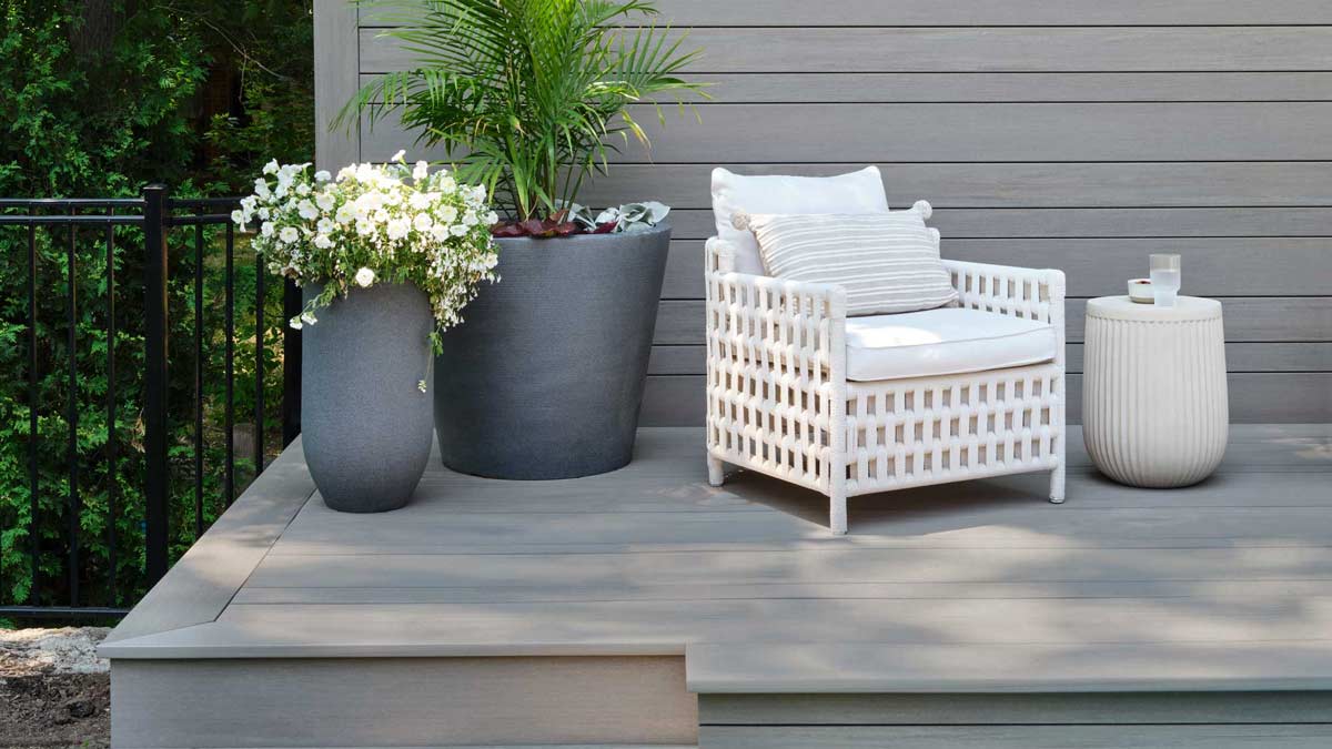 Light gray deck with a matching backboard, two potted plants, an armchair, and a side table