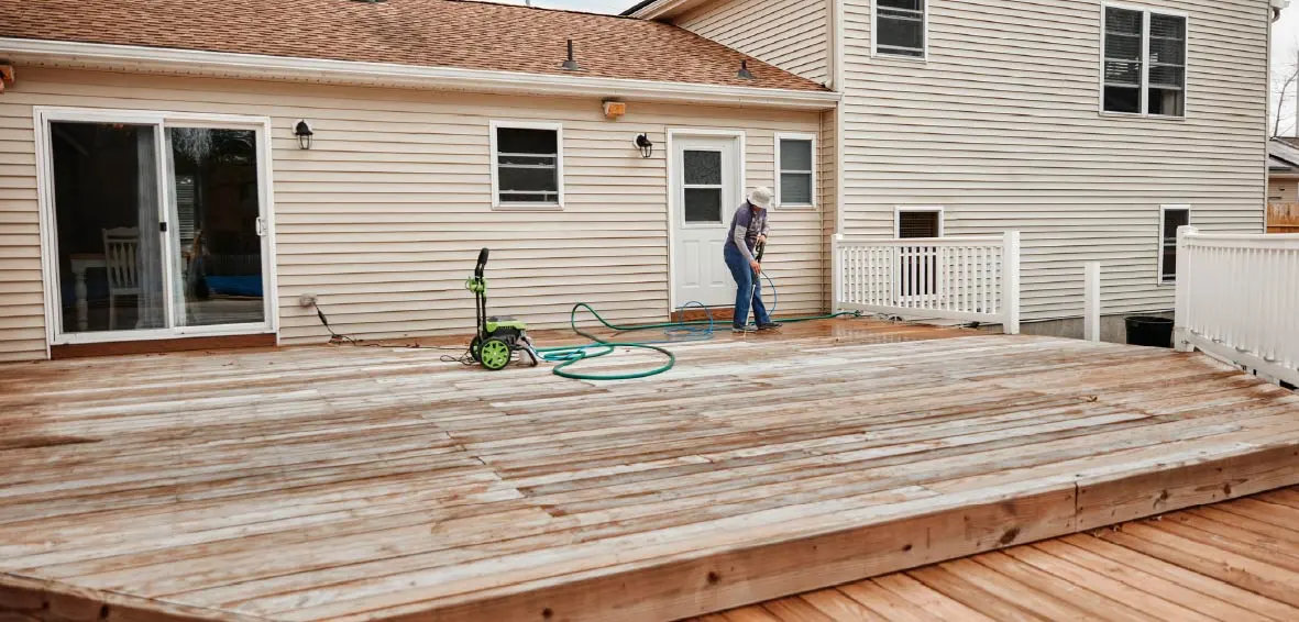 A man using a pressure washer to clean an untreated wood deck.