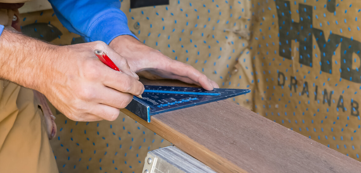 A carpenter marks a measurement at the end of a board using a speed square. 