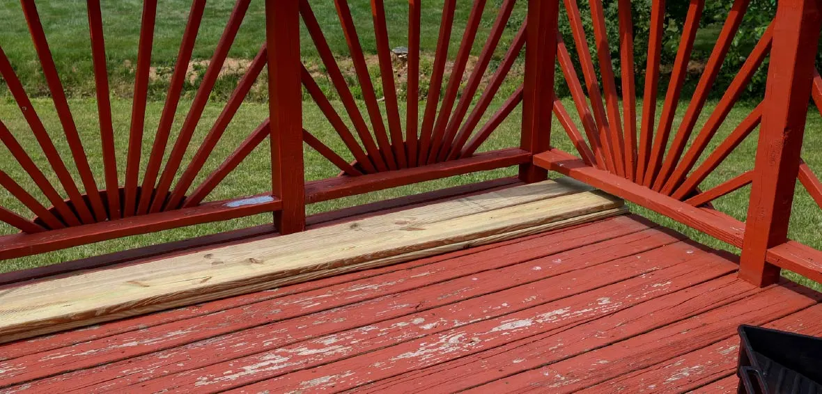 An old red wood deck shows chipping and peeling paint and need maintenance.