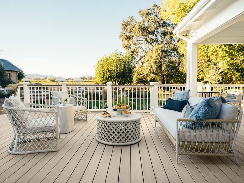 Two modern wicker chairs sit opposite a wicker couch. A coffee table with fruit, cheeses, and wine atop it is in the middle of the furniture, clearly ready to entertain.