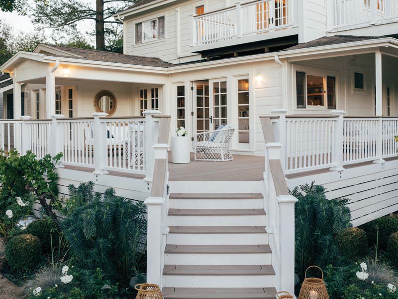 View from the stairway leading up to the first deck on the large white house. Each step uses matching TimberTech Coastline deck boards on the walking surface.