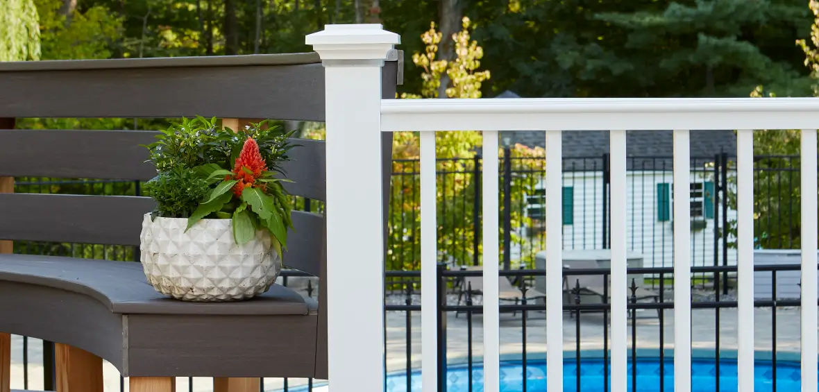 Vertical, square balusters in a white railing connect to a curved bench, a pool's in the background.