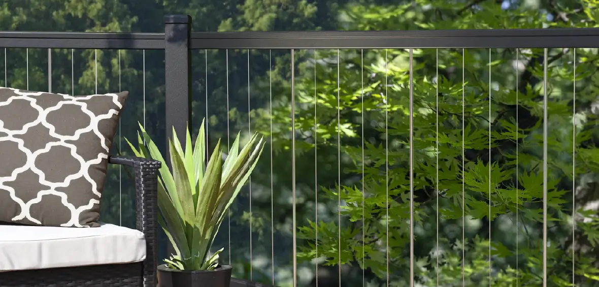 Vertical cable infills with a black aluminum railing on a deck with a chair and plant. 