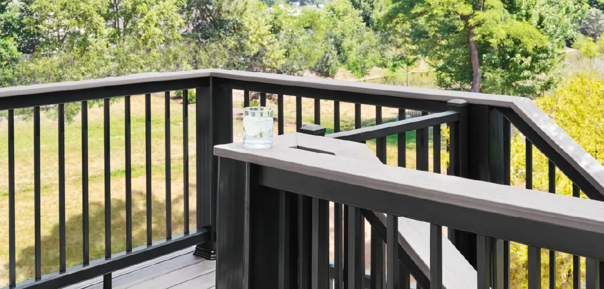 Black railing features a wide drink rail with a glass of water set on top. 