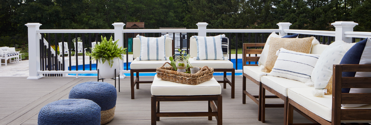 Plush, white outdoor seating on a deck with a patio and pool in the background.