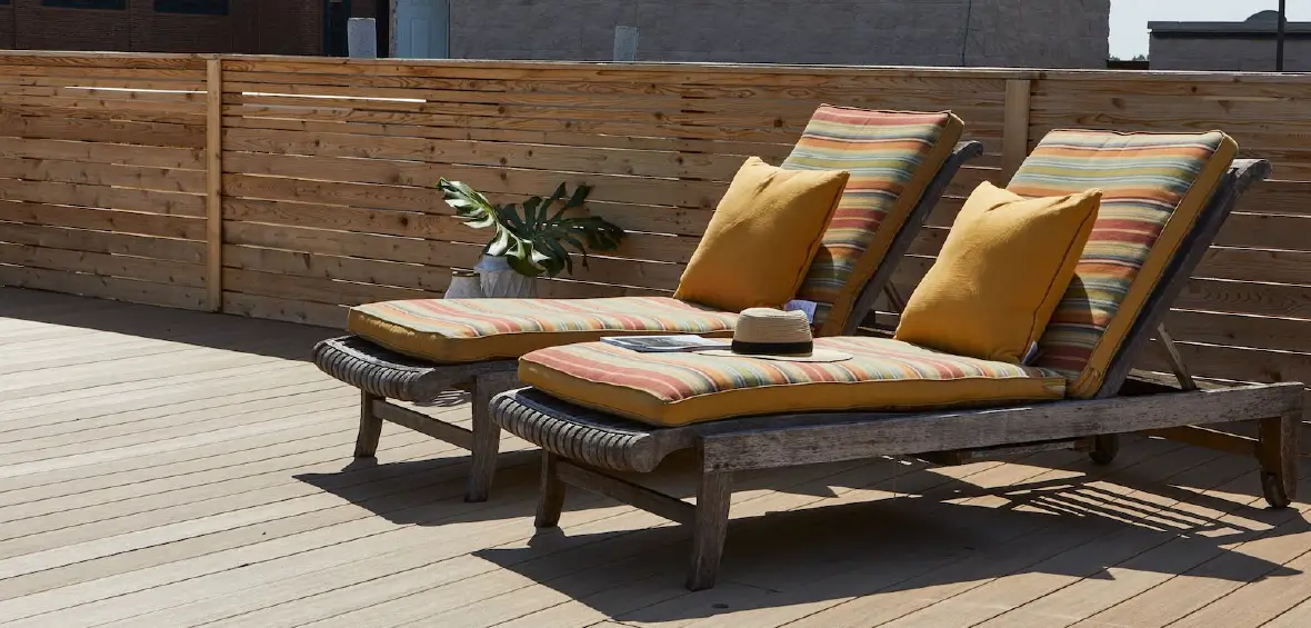 Two lounge chairs on a deck with a privacy railing made of wood slats.