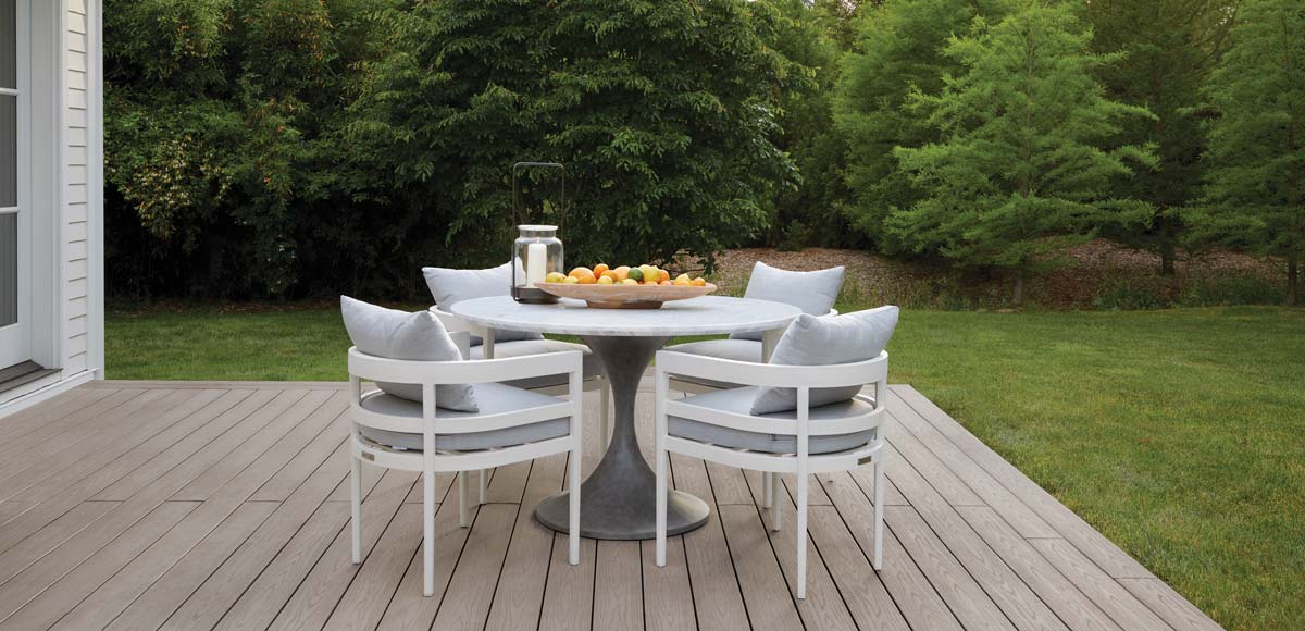 A marble, circular table with four matching chairs with a lantern and fruit bowl on Danny's backyard deck