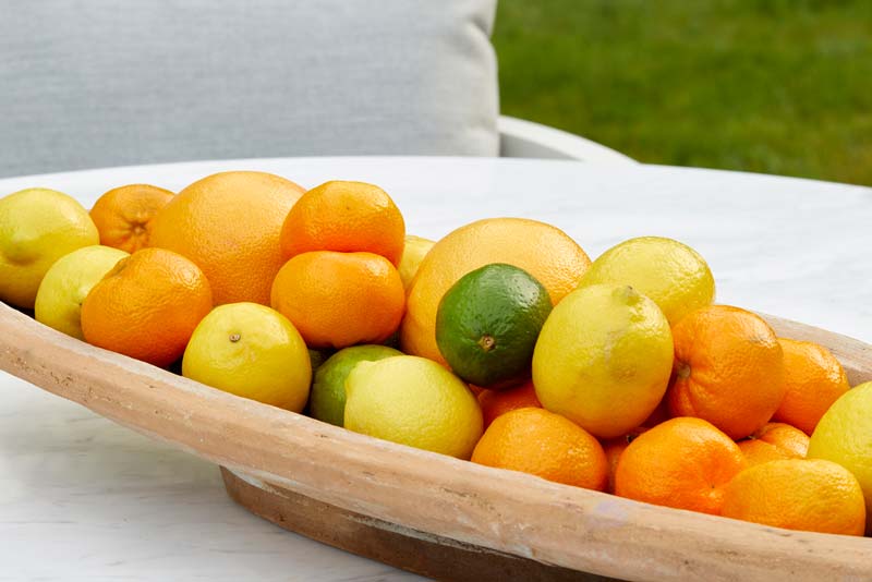 Bowl of colorful fruits including oranges, lemons, and limes on an outdoor patio table