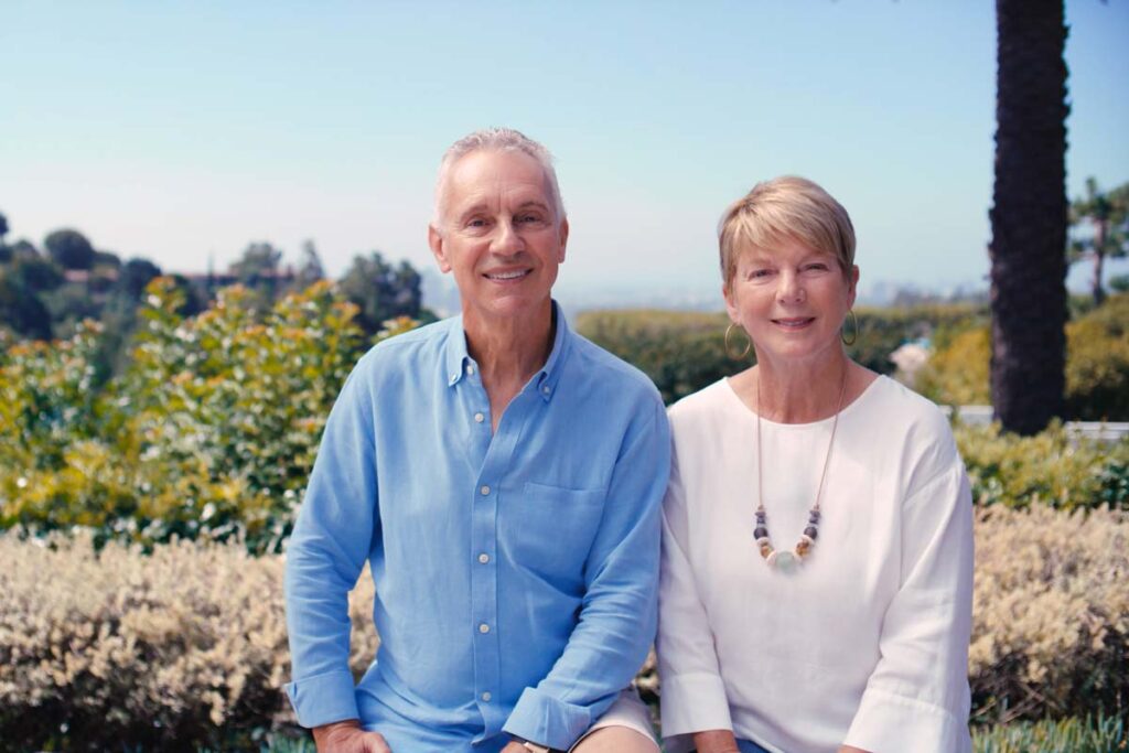 Mark and Jennifer pose for a portrait. The two are surrounded by wildflowers and bushes in the background.