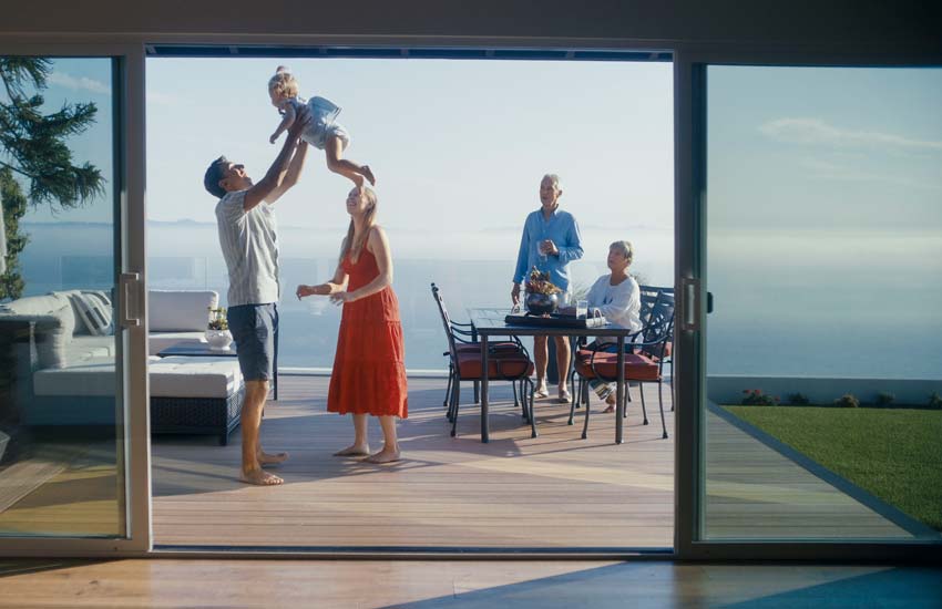 Mark and Jennifer look on as their family members playfully raise a baby into the air on the deck.