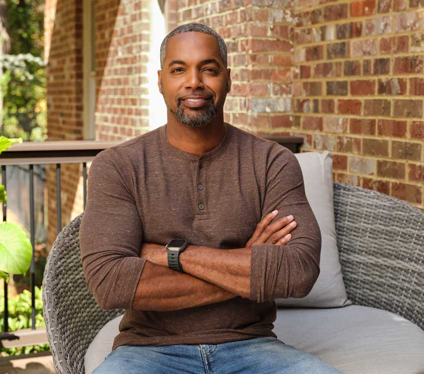 Mike Jackson poses for a headshot on his porch, arms crossed and cracking a smile