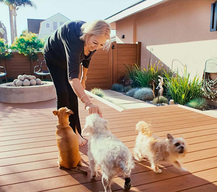 Paddi is smiling and bent over to pet one of her small, blonde dogs