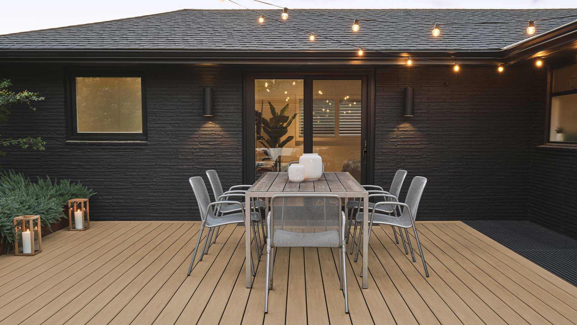 Black painted brick home with a light tan deck and string lights overhead