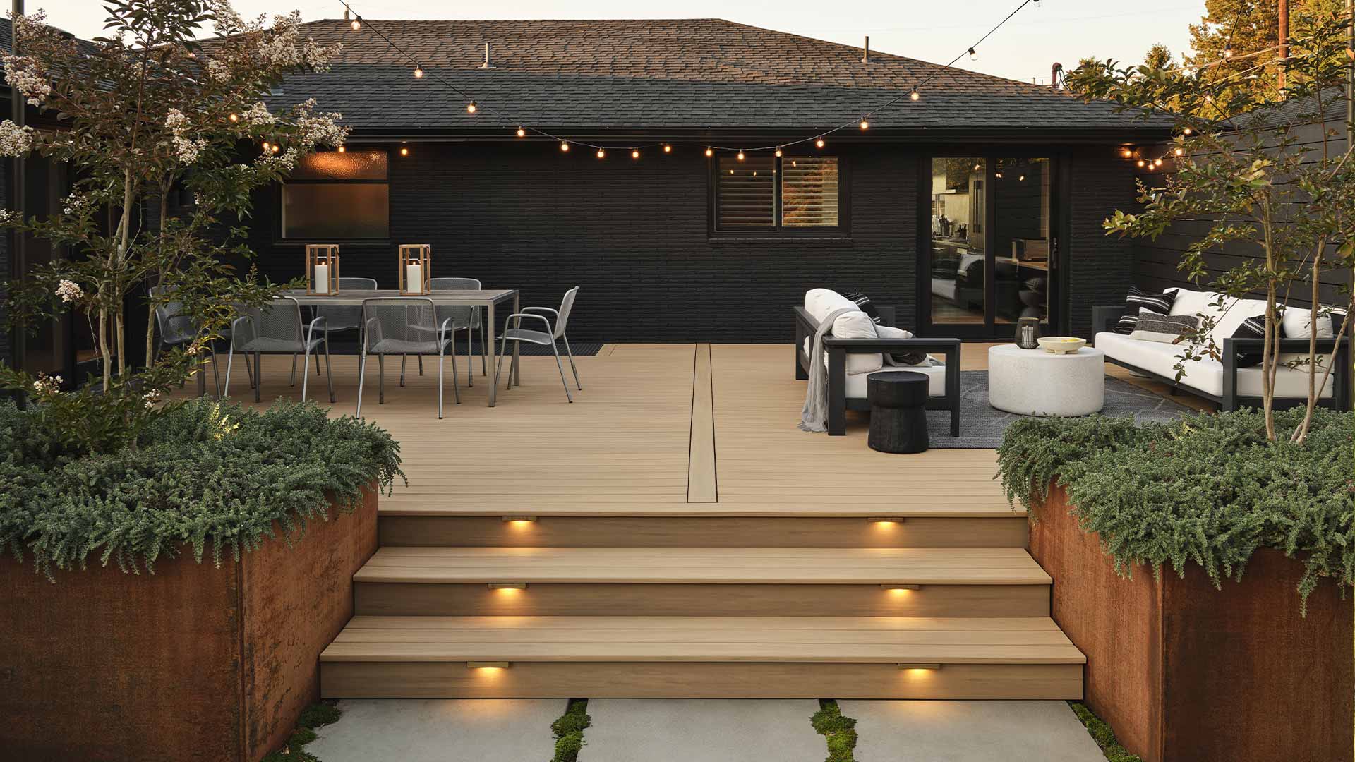 Black brick home with tan deck that has string lights overhead