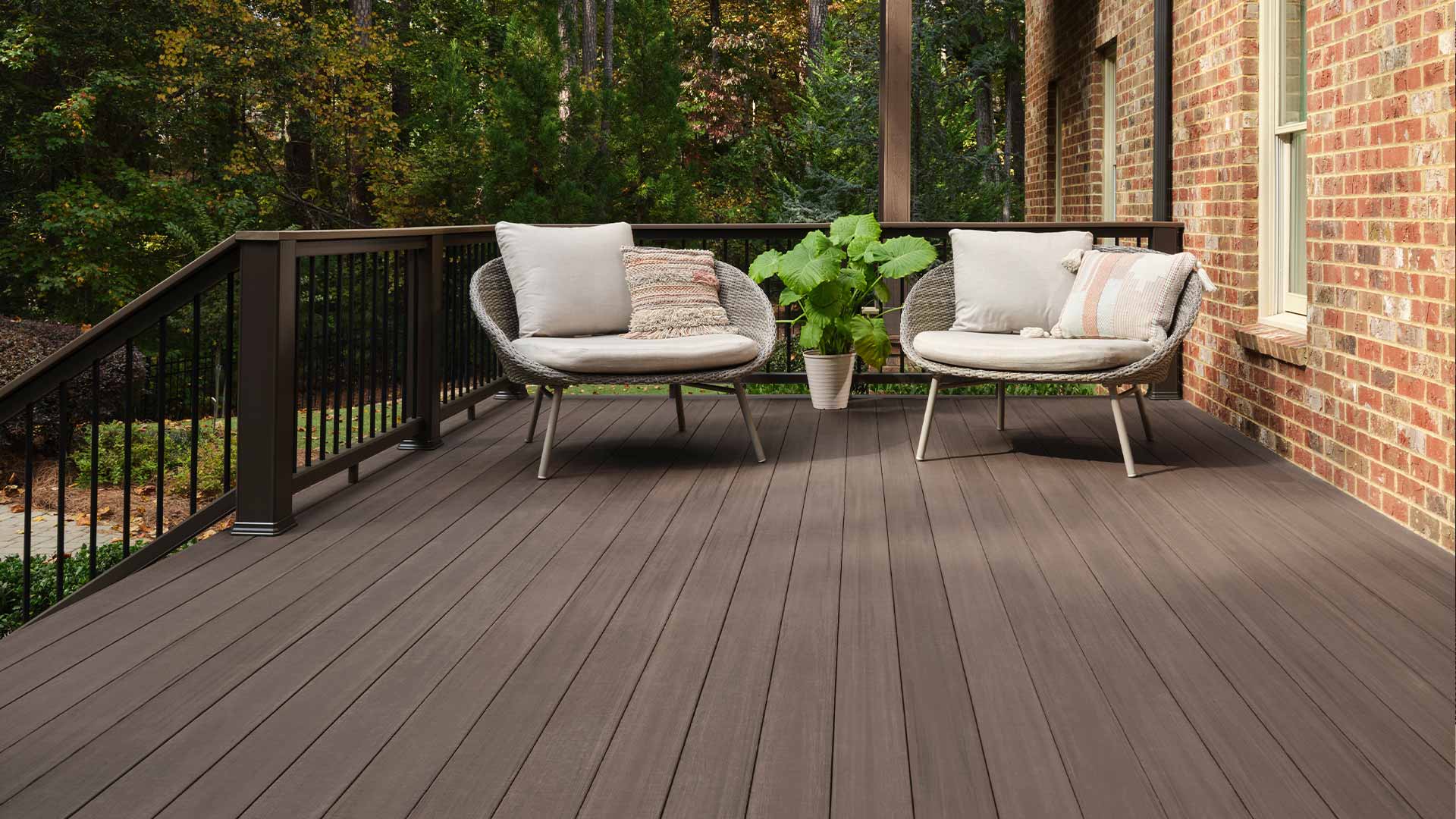 Brown deck with wicker arm chairs and decorative pillows on it
