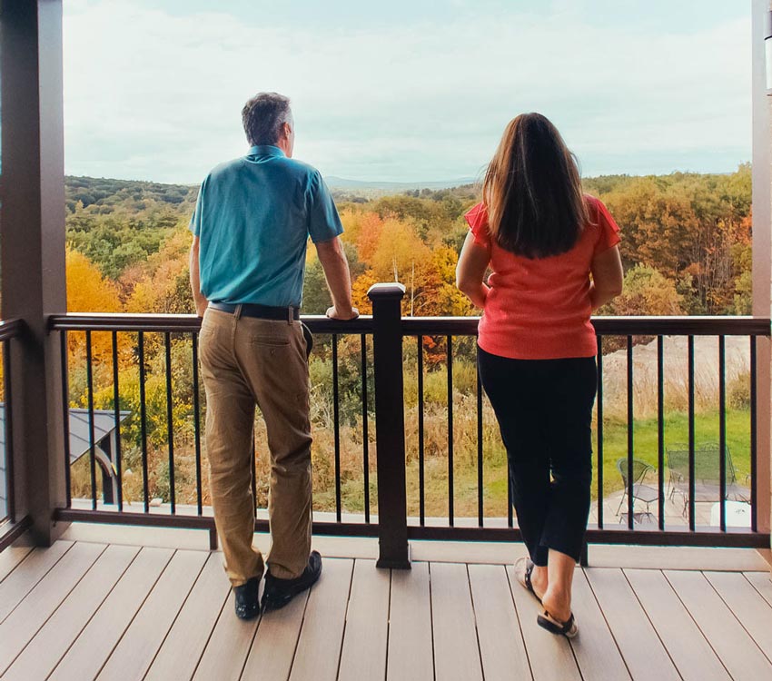 Lori and Mike lean against the railing of their new deck and look out upon the multi colored New England forest in fall