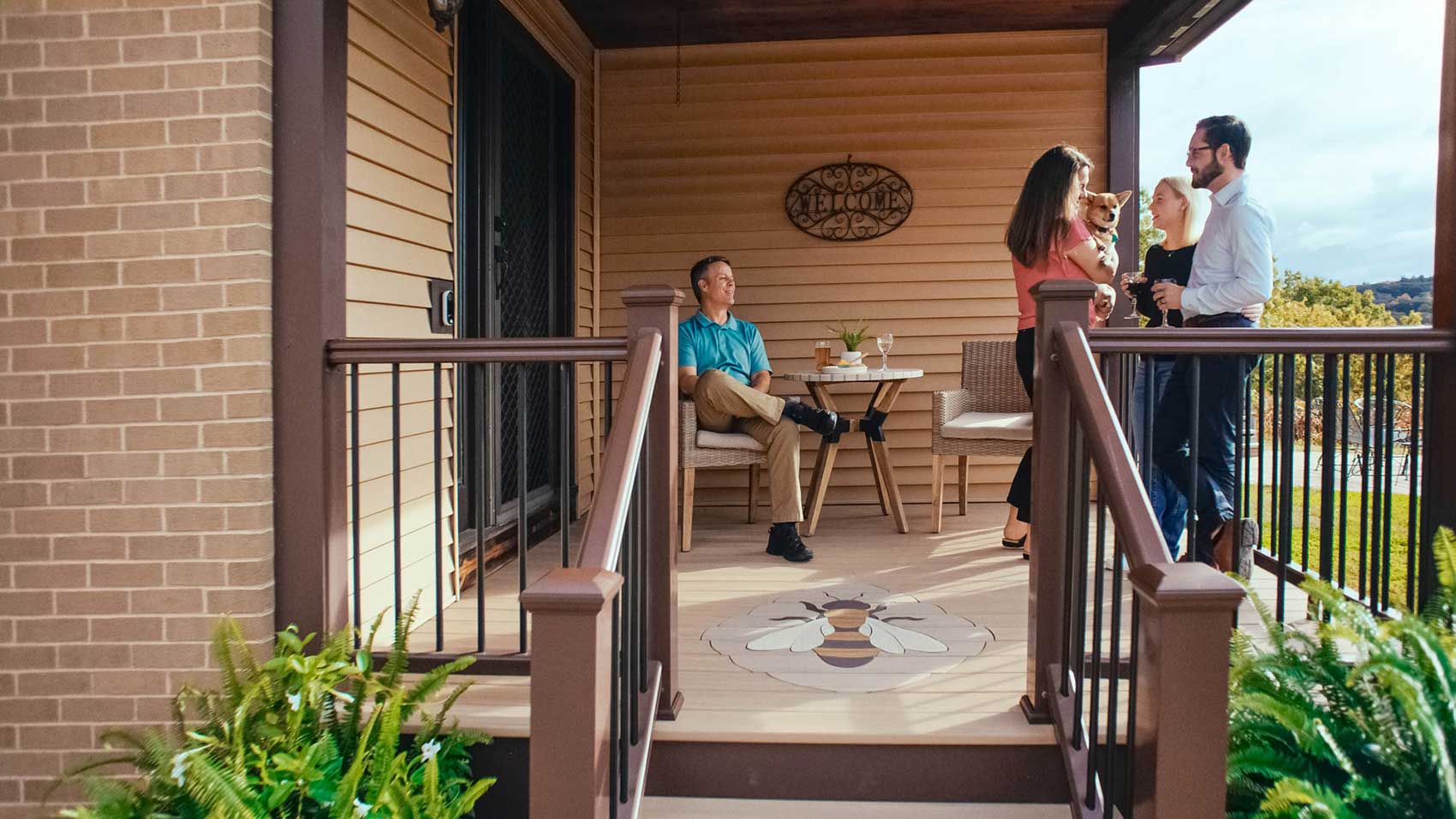 Mike sits on a chair and looks on as Lori holds her pet dog and chats with visitors on their deck