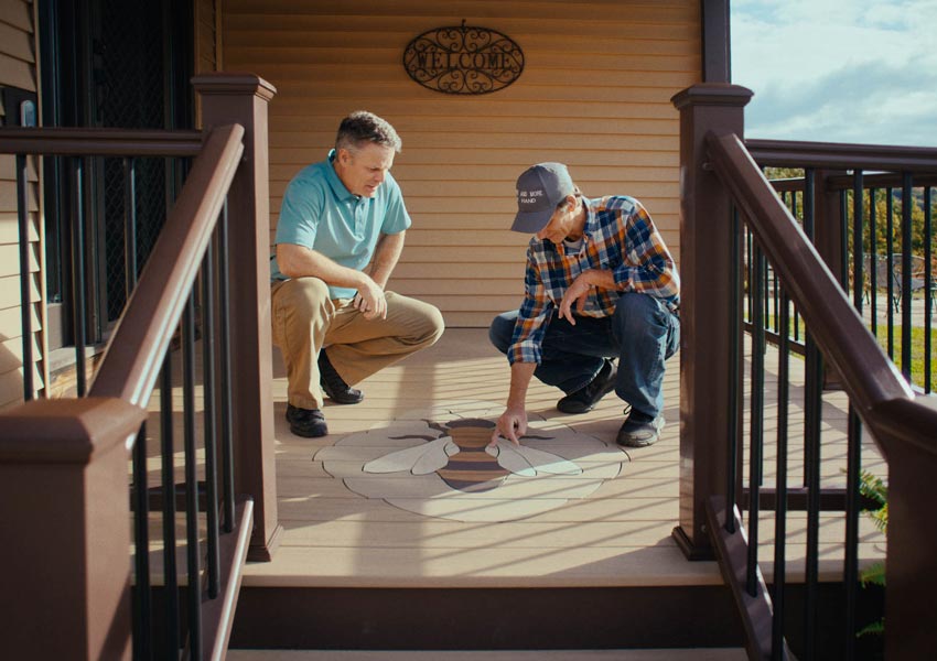 Mike and a friend crouch down to inspect a unique bee design that was built into the surface of their deck