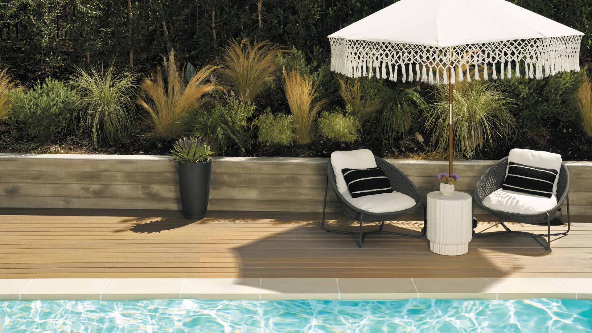 Two wicker chairs under an umbrella on a pool deck built with TimberTech Composite Tigerwood boards