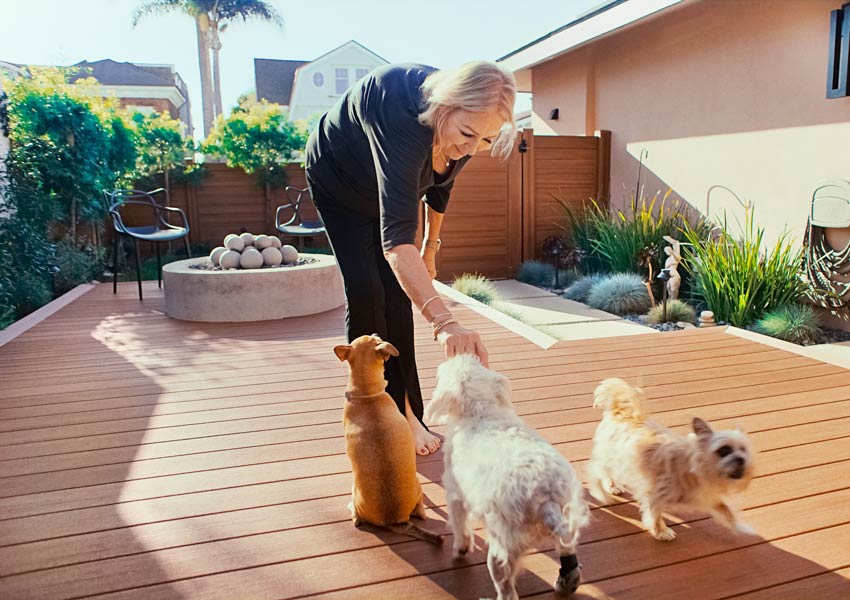 Paddi bends down on her deck to pet her three small dogs