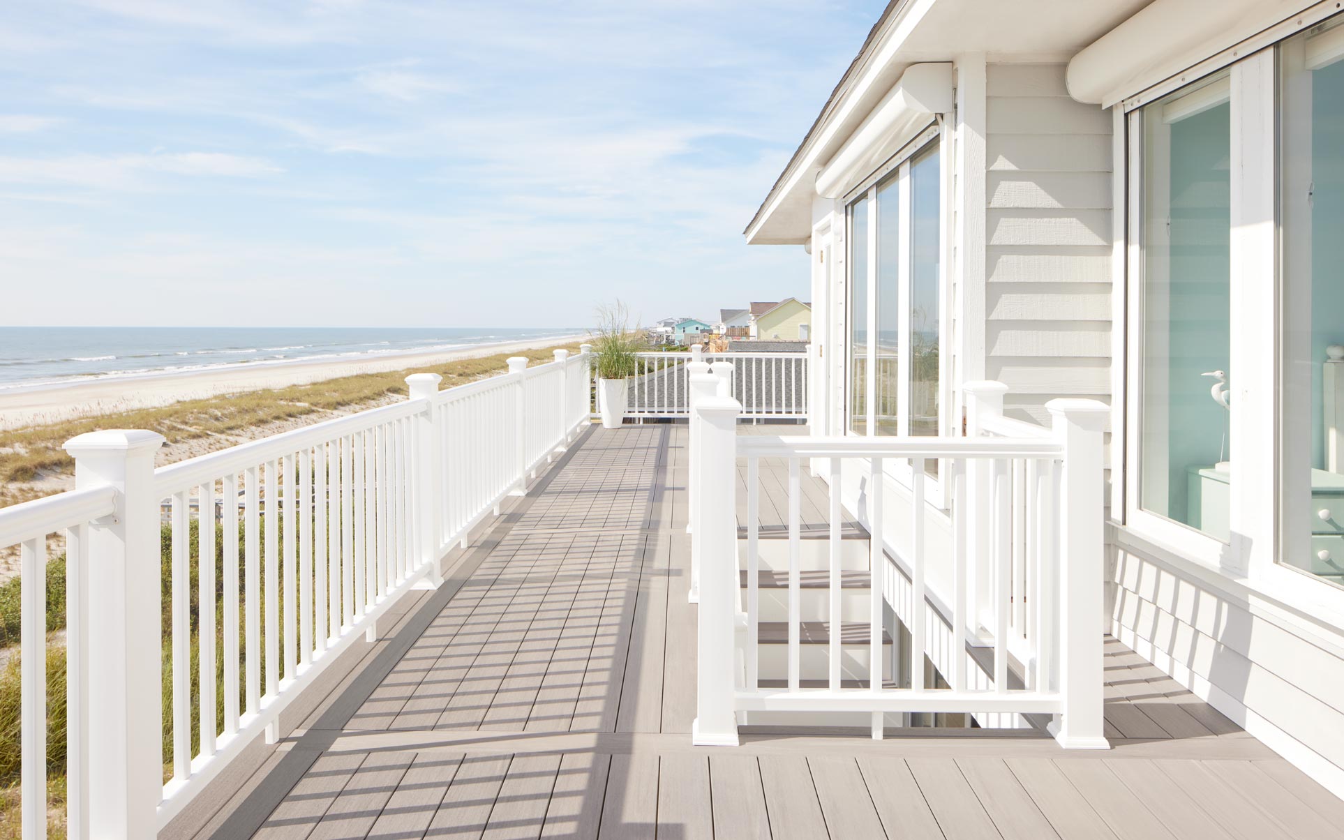 A light gray TimberTech deck that wraps around the back of a beach house with bold, white railing.